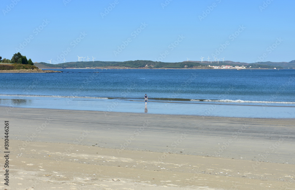 Beach with wet sand, woman and blue sky. Muxia, Spain.