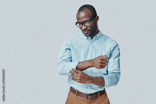 Schilderij op canvas Fashionable young African man adjusting sleeve while standing against grey backg