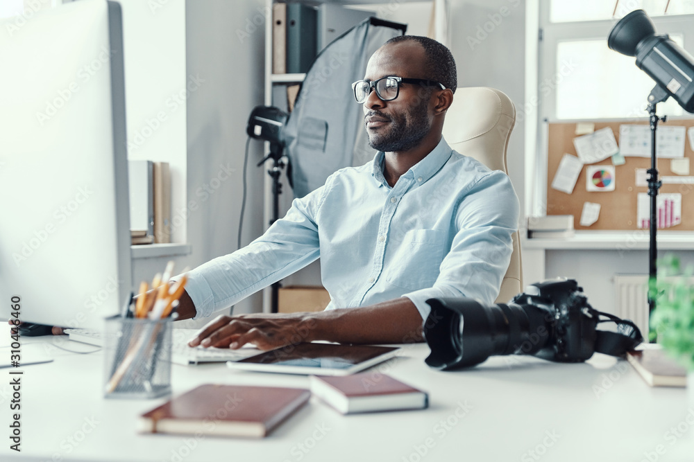 Handsome young African man using computer while working in the modern office Handsome young African man using computer while working in the modern office