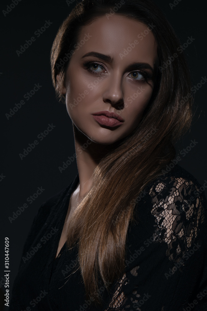Young beautiful woman in black dress with a serious facial expression shot in the studio in the shadows. Studio shot. Young beautiful woman in black dress with a serious facial expression shot in the studio in the shadows. Studio shot.