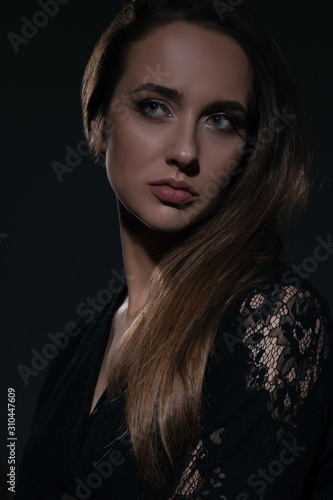 Young beautiful woman in black dress with a serious facial expression shot in the studio in the shadows. Studio shot.