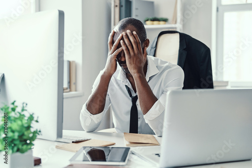 Frustrated young African man in formalwear keeping head in hands head while working in the office photo