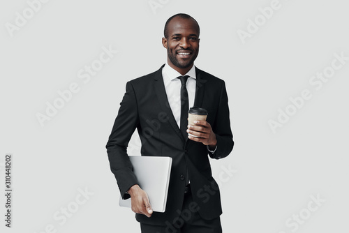 Young African man in formalwear looking at camera and smiling while standing against grey background