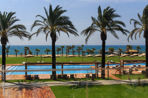 hotel grounds with swimming pool, clear blue sea and trees, summer Sunny day palm trees and sand © Dikkens