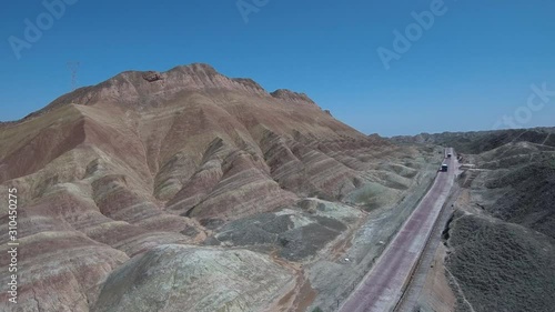 Flying over the main road that leads to the Zhangye Danxia Landform Geological Park known also like the rainbow mountains with the colorful hills on the left and clear blue sky in the background. 