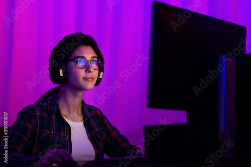 Student girl using computer late at night, wearing headphones