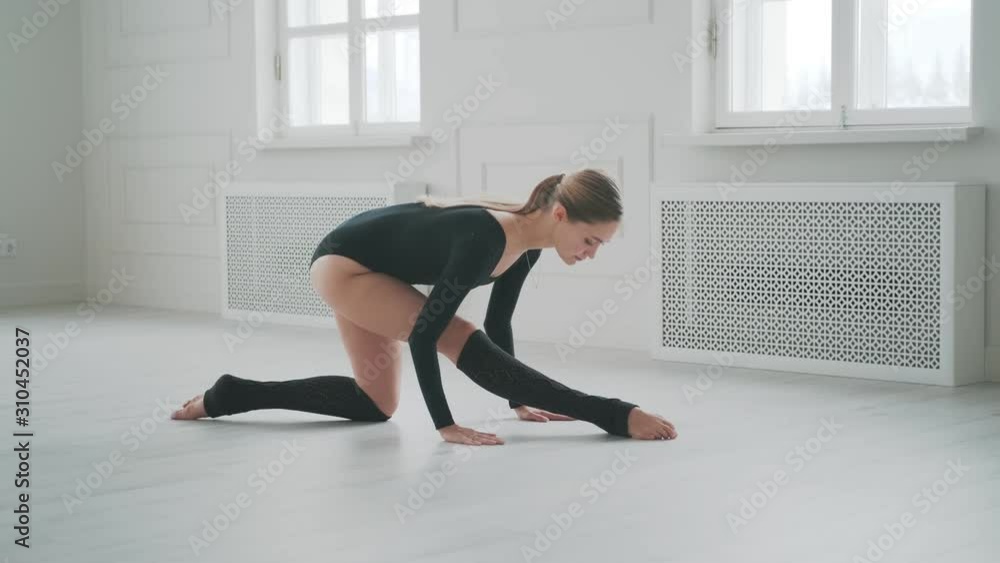 girl in a black bodysuit is warming up in a bright studio. dancer doing stretching sitting on the floor girl in a black bodysuit is warming up in a bright studio. dancer doing stretching sitting on the floor