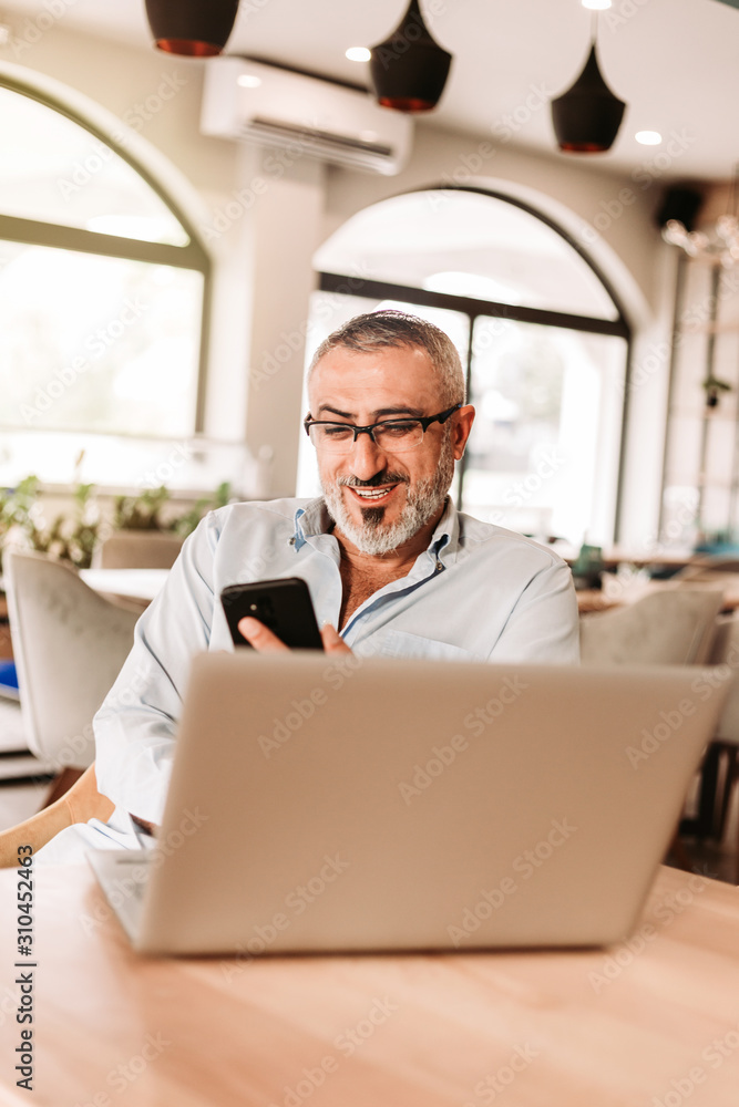 Handsome middle aged man with beard looking at phone in his hand, smiling.