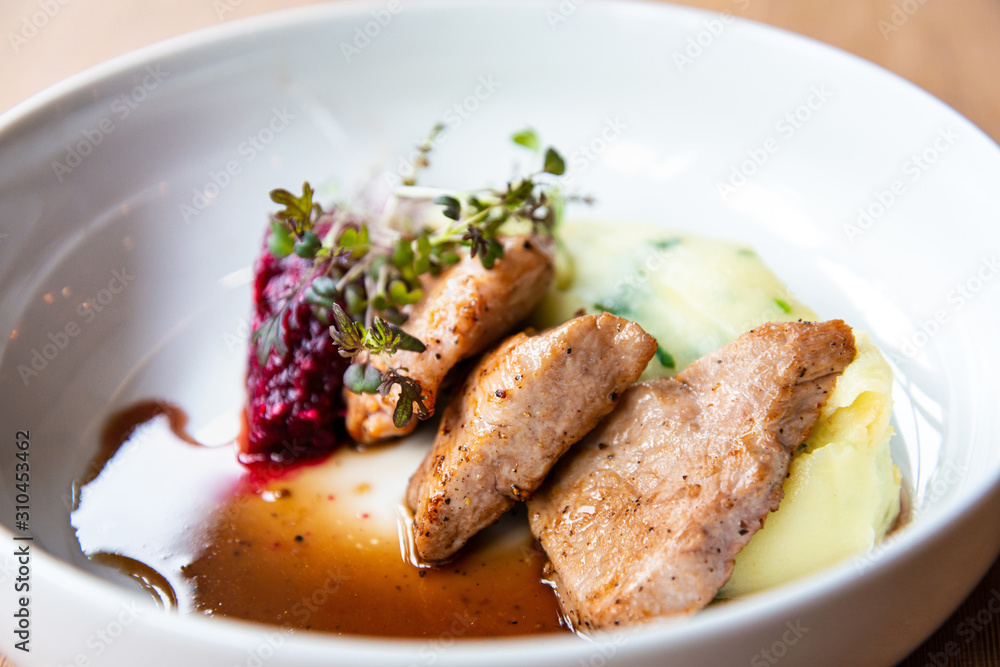 Delicious roasted pork filet cooked with smashed potatoes and smashed beetroots served in white plate.