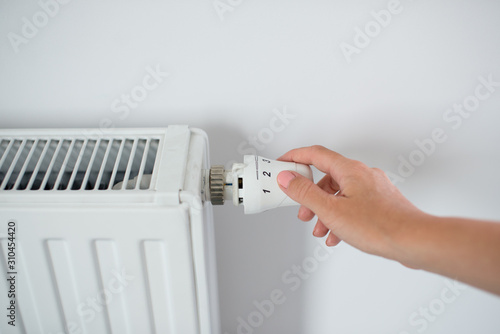 Woman Hand Adjusting The Knob Of Heating Radiator. The valve from the radiator - Heating. Hand adjusting thermostat valve of heating radiator in a room. Copy space.