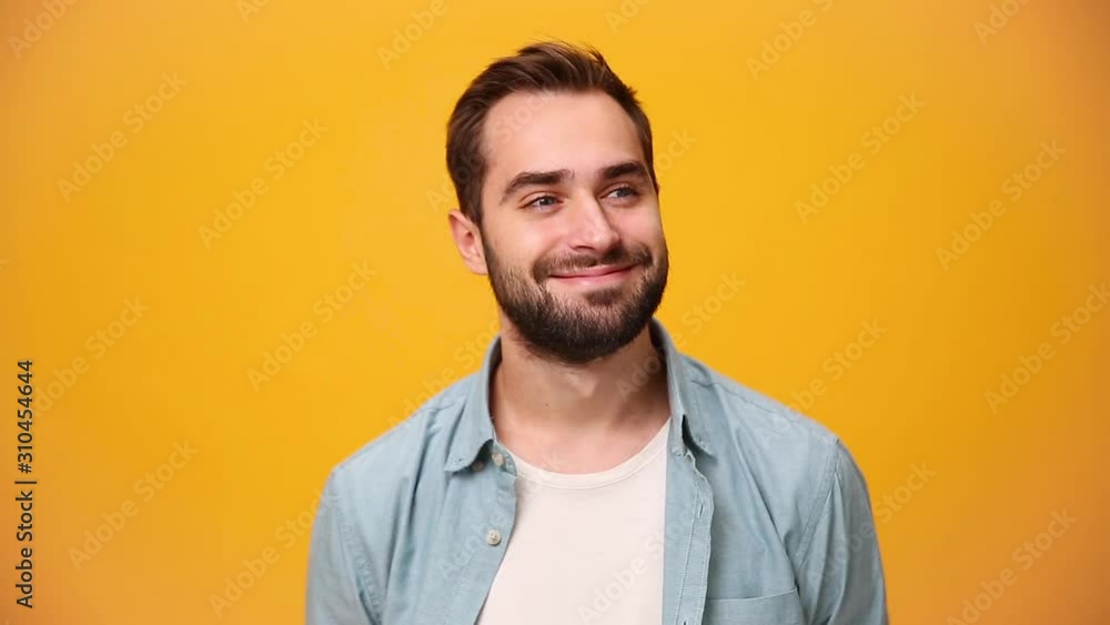 Handsome dreamful bearded young guy 20s in denim shirt white t-shirt isolated over yellow background in studio. People sincere emotions, lifestyle concept. Looking at the camera with charming smile. Handsome dreamful bearded young guy 20s in denim shirt white t-shirt isolated over yellow background in studio. People sincere emotions, lifestyle concept. Looking at the camera with charming smile.