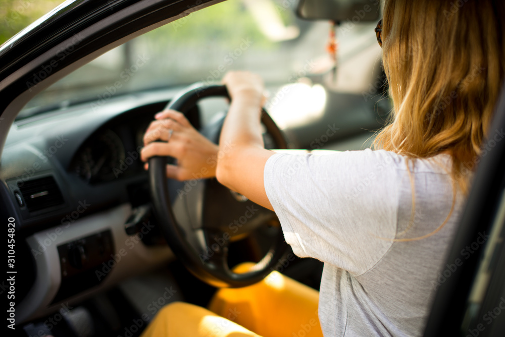 Young beautiful blonde hair girl with driving a car. Confident and beautiful. Rear view of attractive young woman in casual wear looking forward her while driving a car.