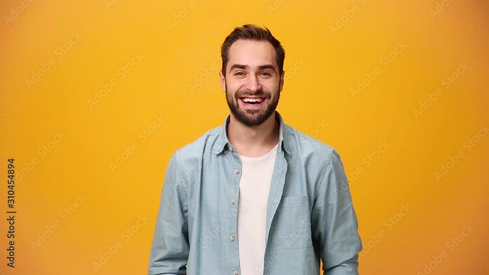 Handsome unshaven bearded young guy 20s in denim shirt white t-shirt isolated over yellow background in studio. People sincere emotions, lifestyle concept. Looking at the camera with charming smile. Handsome unshaven bearded young guy 20s in denim shirt white t-shirt isolated over yellow background in studio. People sincere emotions, lifestyle concept. Looking at the camera with charming smile.