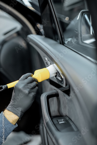Worker provides a professional vehicle interior cleaning, wiping door panel with a brush at the car service station, close-up view © rh2010
