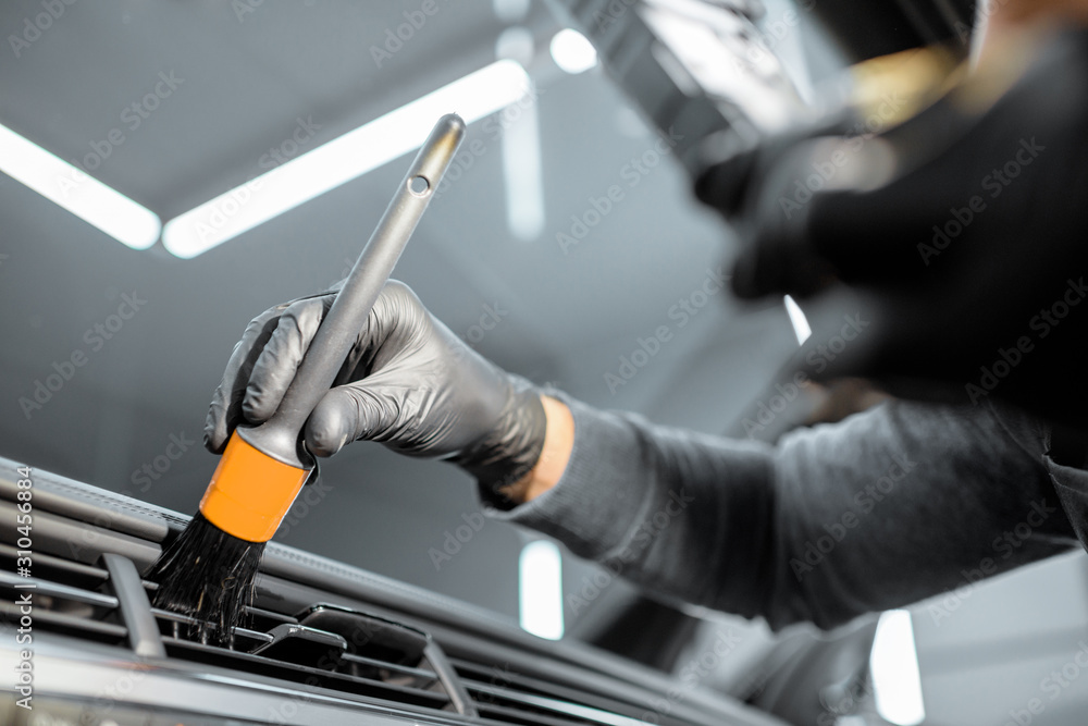 Worker provides a professional vehicle interior cleaning, wiping indoor front panel with a brush at the car service station, close-up
