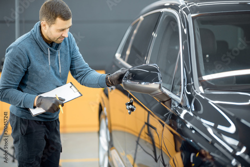 Car service worker examining vehicle body for scratches and damages, taking a car for professional auto detailing. Professional body car inspection concept