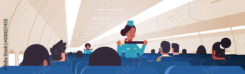 stewardess explaining passengers how to use seat belt fastening in emergency situation african american flight attendants in uniform safety demonstration concept airplane board interior horizontal