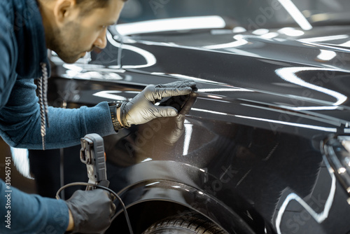 Obraz na plátně Car service worker examining vehicle body for scratches and damages, taking a car for professional auto detailing