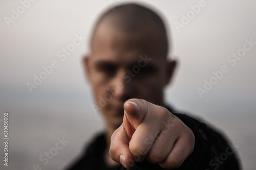 The bald brutal guy points to the camera with his index finger. Forefinger in the foreground, the defocused face of the guy in the background. Pointing to something or someone.