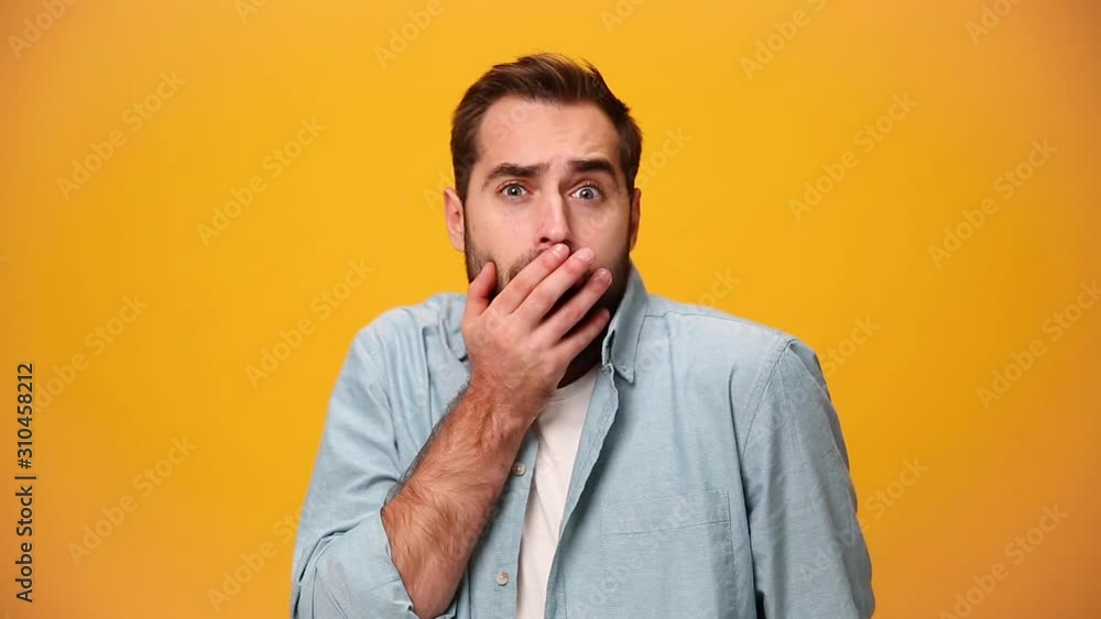 Shocked bearded young guy 20s in denim shirt white t-shirt isolated over yellow background in studio. People sincere emotions, lifestyle concept. Looking at camera with scared look, fearful glance. Shocked bearded young guy 20s in denim shirt white t-shirt isolated over yellow background in studio. People sincere emotions, lifestyle concept. Looking at camera with scared look, fearful glance.