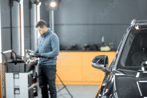 Car service worker preparing for vehicle body detailing at the modern automotive service box. Image focused on the car window