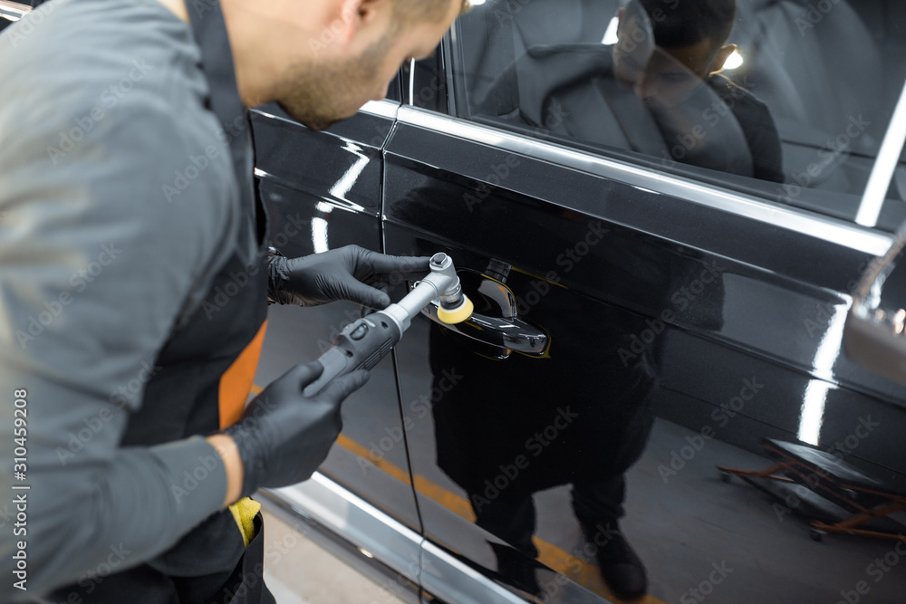 Car service worker polishing vehicle door handle with special wax from scratches. Professional car detailing and maintenance concept
