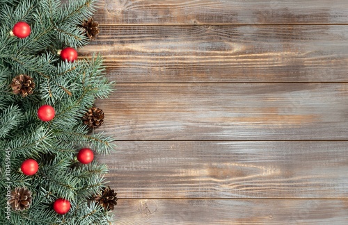 Christmas border with fir branches, red balls and cones on a wooden background.