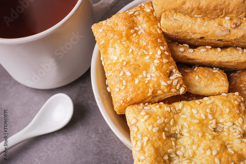 Freshly prepared puff pastry with sesame seeds close-up in a white plate and a cup of black tea. Details The concept of home baking, breakfast, snack. photo