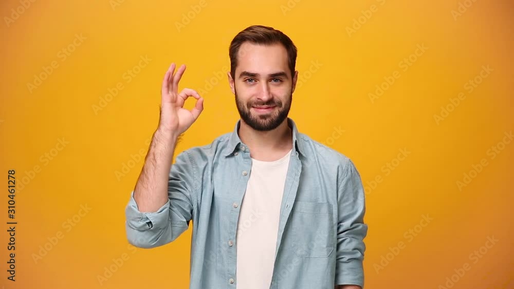 Handsome bearded young guy 20s in denim shirt white t-shirt isolated over yellow background in studio. People sincere emotions, lifestyle concept. Looking at the camera with smile, showing OK gesture Handsome bearded young guy 20s in denim shirt white t-shirt isolated over yellow background in studio. People sincere emotions, lifestyle concept. Looking at the camera with smile, showing OK gesture