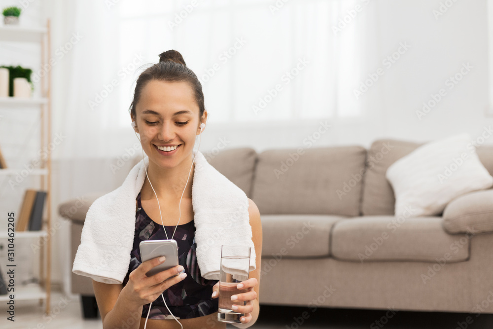Smiling girl with water and phone after exercising at home