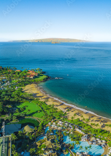Vertical, portrait orientation drone picture showing the beautiful coast line and beaches of Wailea, Maui, Hawaii. Molokini can be seen in the distance. A crescent shaped volcanoe island.
