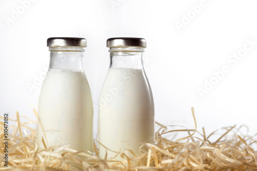 Bottles of fresh milk in the hay isolated on white. Close-up.