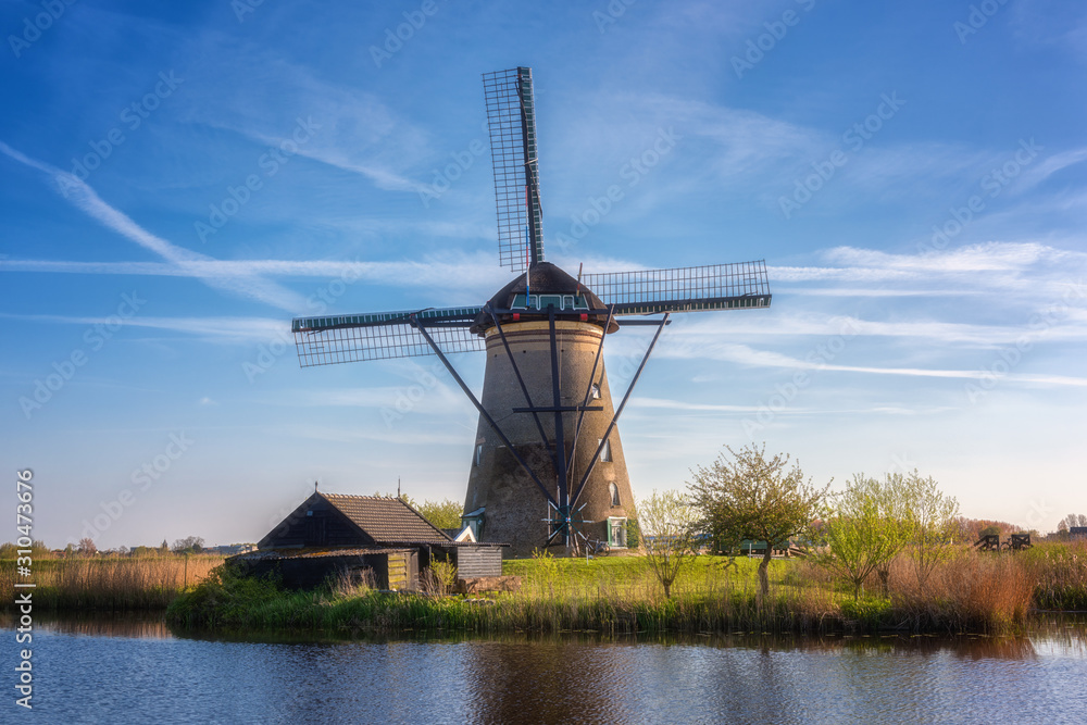 Famous Kinderdijk village of mills, popular tourist attraction in Netherlands (Holland), outdoor travel background. Scenic landscape with windmill, water, green grass and blue sky with clouds