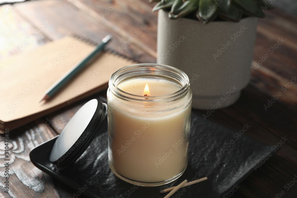 Burning candle in glass jar, succulent and notebook on wooden background, close up - obrazy, fototapety, plakaty 