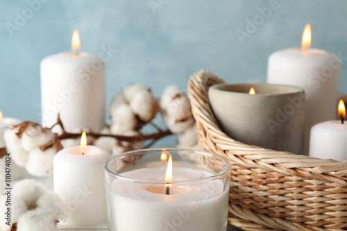 Burning candles  basket and cotton against blue background  close up