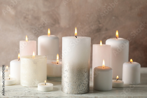 Different burning candles against brown background, close up