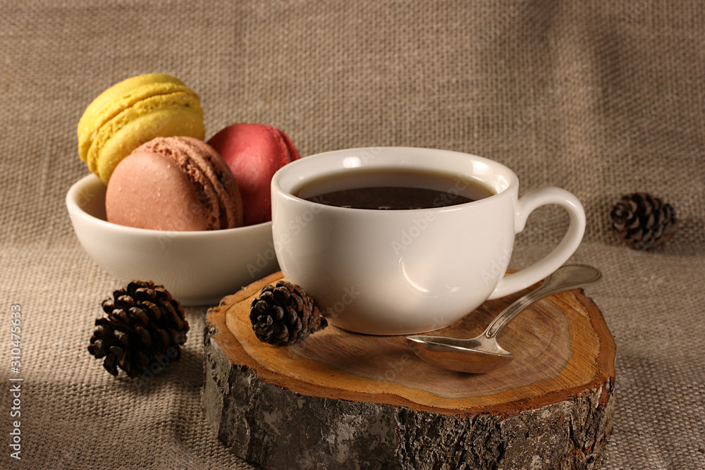 Cup with tea and a spoon on a wooden stand on a background of brown, red and yellow cookies Cup with tea and a spoon on a wooden stand on a background of brown, red and yellow cookies