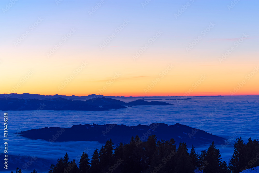 Colorful sky at sunset. Hills and forest sticking out of fog. Austria, Switzerland. Copy space