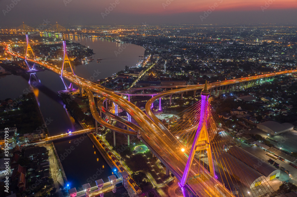 Evening bridge with lights on the bridge over the Chao Phraya River. Aerial view of the Bhumibol Adulyadej Suspension Bridge over the Chao Phraya River in Bangkok with cars on the bridge at the sunset
