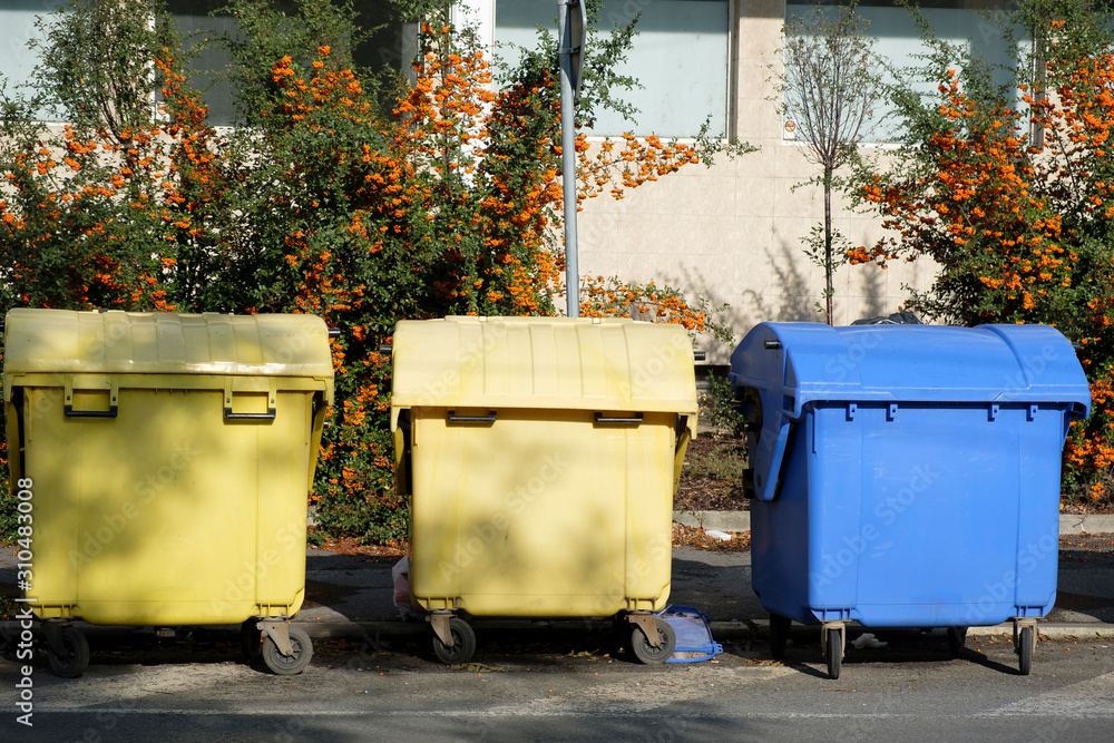 Three closed dumpsters on the edge of a paved road Three closed dumpsters on the edge of a paved road