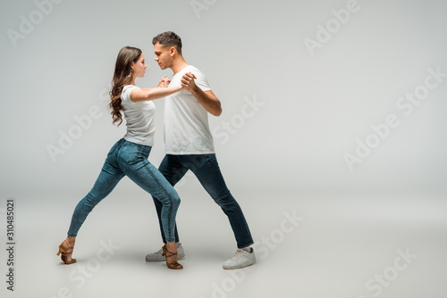 side view of dancers in t-shirts and jeans dancing bachata on grey background