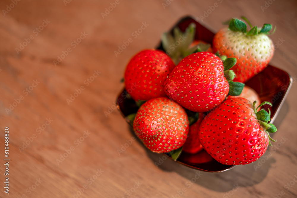 Fresh red strawberries in the copper bowl  on the wooden background