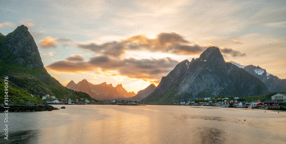 Panorama shot of Reine in Lofoten Islands in Norway during sunset. Warm tones and colors fills the cloudy sky during summertime. Travelocity and traveling concept.