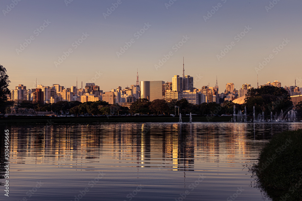 Fim de tarde em São Paulo, com reflexo em lago ao entardecer.