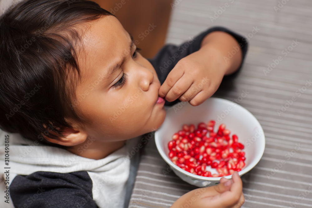 Pre-school age boy with hand dexterity self feeding from a bowl of pomogranate seeds.