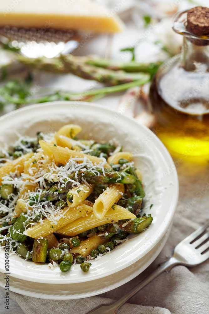 Penne pasta with green asparagus and peas sprinkled with grated Parmesan cheese, close up