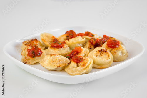 Russian food pelmeni, fried meat dumplings on white plate, with tomato sauce, isolated