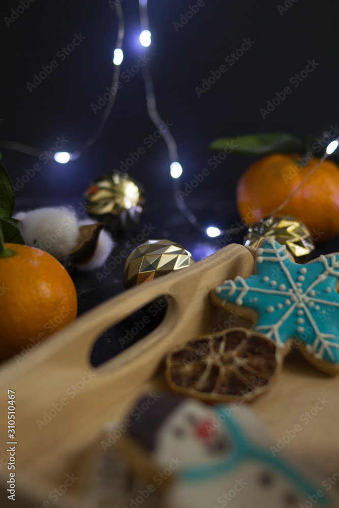Christmas cookies in the shape of a house, a snowman and stars lie in the gap with fresh orange juice in a glass of farm-style drink. Around nuts, cinnamon, decor. Black background.
