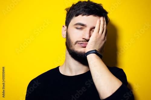 Studio portrait of young man, holding hand on face, feeling tired, background of yellow color.