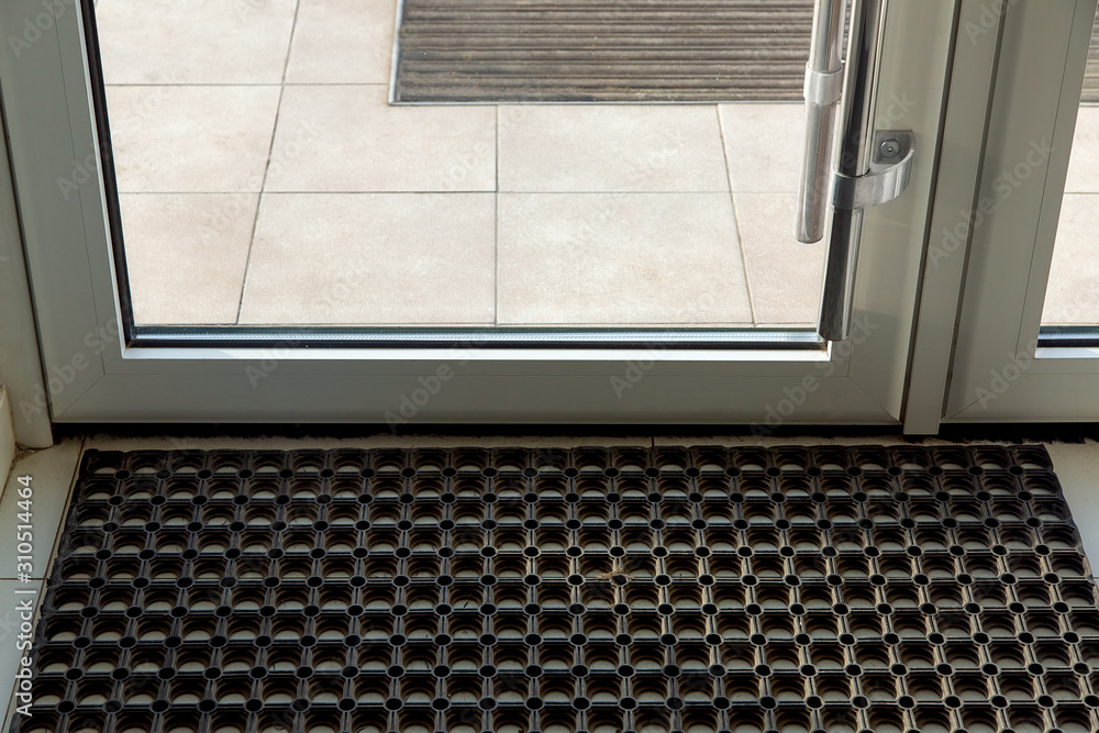 threshold with a rubber foot mat in the front glass door of the office with tiles on the floor close up. threshold with a rubber foot mat in the front glass door of the office with tiles on the floor close up.
